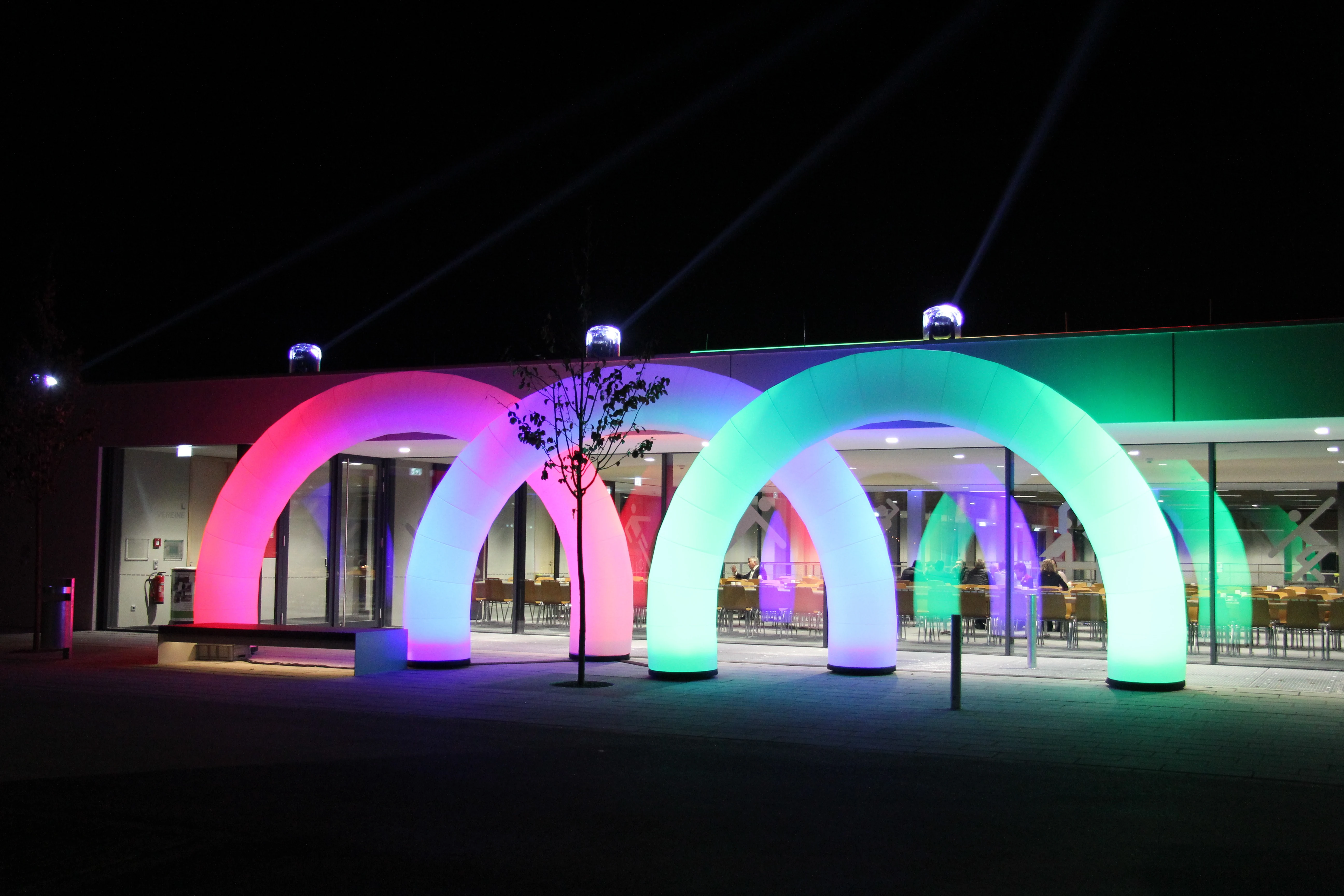 Beleuchtete LED-Torbögen in Regenbogenfarben vor der Sporthalle Stadtbergen bei Nacht